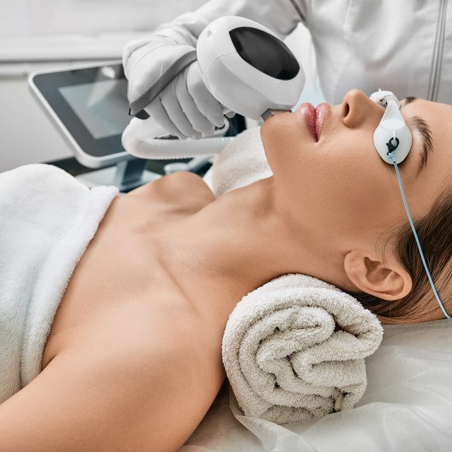 Photorejuvenation, rosacea treatment, removing brown spots and vascular mesh. Cosmetologist using IPL apparatus treats skin of female patients face